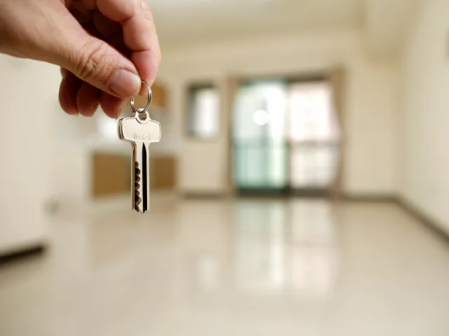 Hand holding a key in front of an empty rental property, symbolising letting and property tax.